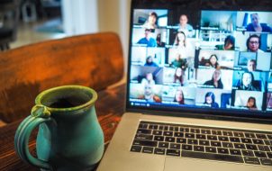 timer for zoom presentation A laptop displaying a grid view of a virtual meeting with multiple participants on screen, alongside a turquoise ceramic mug on a wooden table.
